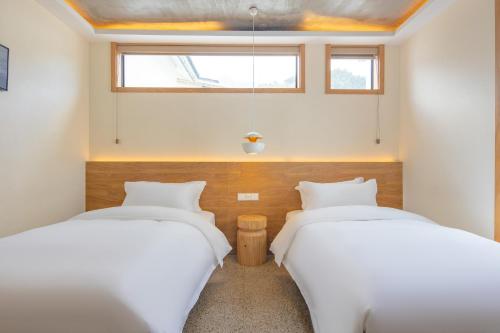 two beds in a room with white sheets and a window at Yunshan Villa in Huangshan Scenic Area