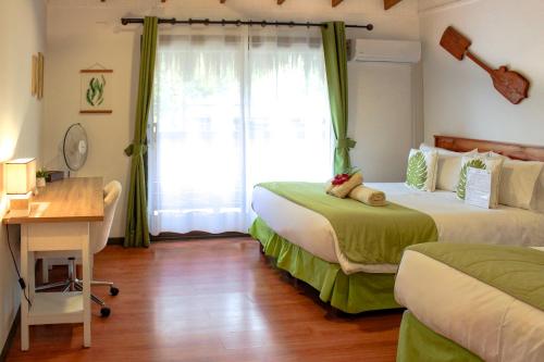 a bedroom with two beds and a desk and a window at Hare Nua Hotel Boutique in Hanga Roa