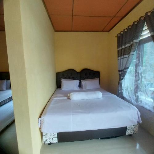 a bedroom with a bed with white sheets and a window at Donny Guesthouse in Tuk Tuk