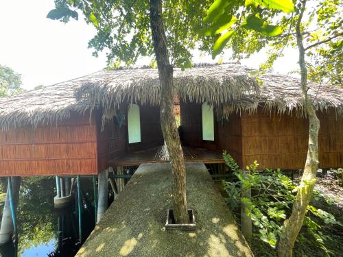 a house with a thatched roof with a tree in front at Villa Baan Pak Pra in Ban Pak Pra (1)