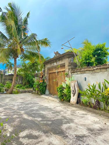 a house with a wooden gate and a palm tree at Joglo Breeze Guesthouse and Villa in Tabanan
