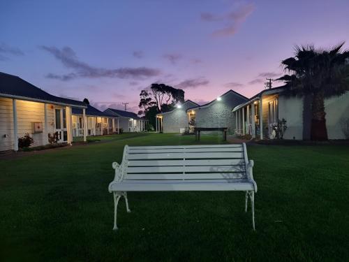 a white bench sitting in the grass in front of houses at The Furlong in Hawera