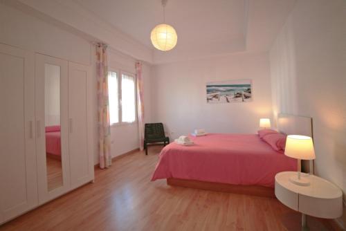 a bedroom with a pink bed and a table and lamp at Apartamentos Bahía Alicante in Alicante