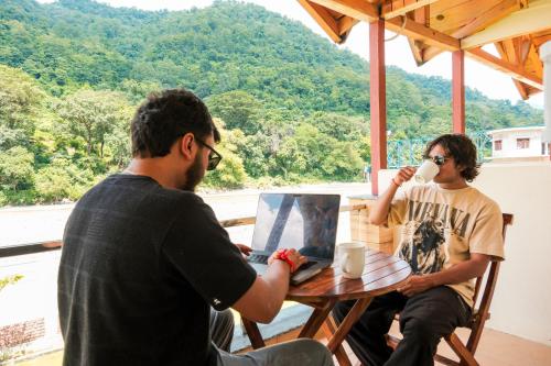two men sitting at a table with a cup of coffee at Qcent Woods Resort & Spa, Rishikesh in Rishīkesh