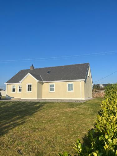 a yellow house with a black roof on a yard at Cúlú in Kincasslagh