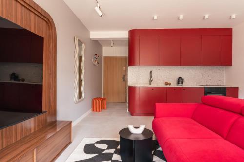 a living room with a red couch and a kitchen at Apartament KOPENHAGA - nowoczesny i stylowy apartament w centrum miasta z miejscem parkingowym in Nowy Targ