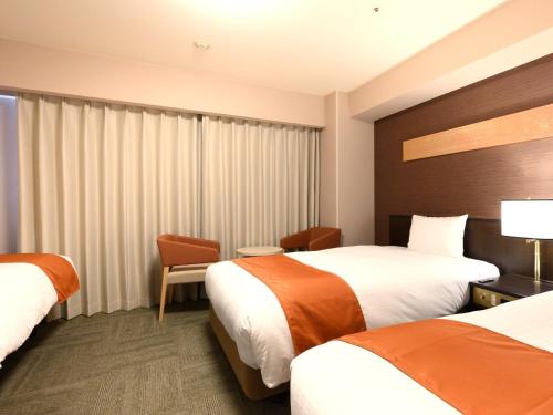a hotel room with two beds and a window at Smile Hotel Premium Kanazawa Higashiguchiekimae in Kanazawa