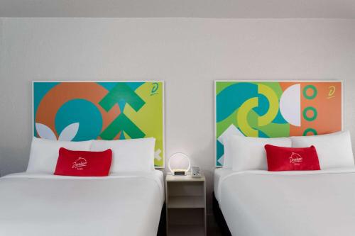 two white beds with red pillows in a room at Travelodge by Wyndham Orlando Lake Buena Vista South in Kissimmee