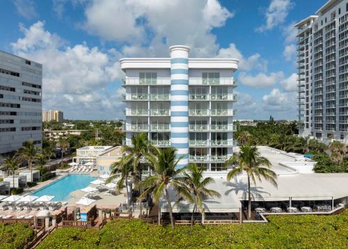 a hotel with a swimming pool and palm trees at The Singer Oceanfront Resort, Curio Collection by Hilton in Palm Beach Shores