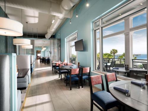 a dining room with tables and chairs and windows at The Ellie Beach Resort Myrtle Beach, Tapestry By Hilton in Myrtle Beach