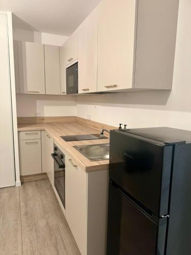 une cuisine avec des armoires blanches et un réfrigérateur noir dans l'établissement Studio moderne et tout équipé, proche du RER, Paris & aéroport d'Orly en 20 min, lit bébé sur demande, à Vitry-sur-Seine
