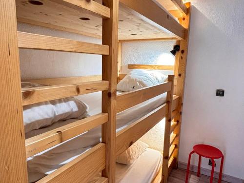 Cette chambre comprend des lits superposés en bois avec un tabouret rouge. dans l'établissement Appartement rénové 2 pièces, accès direct aux pistes et proche centre station - FR-1-634-75, à Morzine