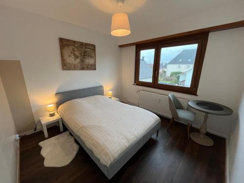 Un dormitorio con una cama y una mesa y una ventana. en Appartement de 115m2 à 10 min de Strasbourg & 25 min d'Europa Park !, en Illkirch-Graffenstaden