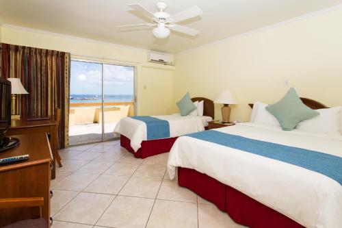 two beds in a hotel room with a view of the ocean at Cara Hotels Trinidad in Claxton Bay