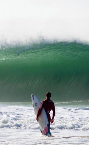 a man walking into the ocean with a surfboard at HM - HouseMirage in Paço de Arcos