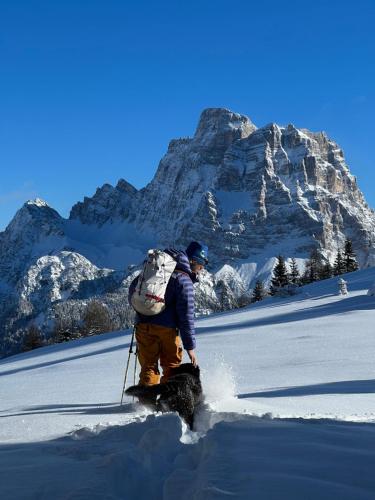 a man with a backpack and a dog in the snow at Climb house Geremia in Selva di Cadore