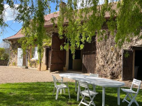 une table et des chaises blanches devant un bâtiment dans l'établissement Les Granges De Semur-en-brionnais With Heated Poo, à Semur-en-Brionnais