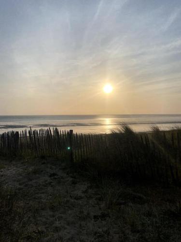 un coucher de soleil sur une plage avec l'océan et une clôture dans l'établissement Chez Fanfan à 150m de la mer, à Hauteville-sur-Mer