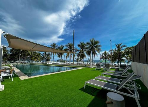 a swimming pool with chairs and a lawn with palm trees at Ocean Front, Luxurious Condo in Downtown Jaco! in Jacó