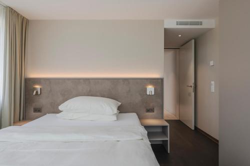 una camera da letto con un grande letto bianco e due luci di Amanthos Living Zürich Airport a Glattbrugg