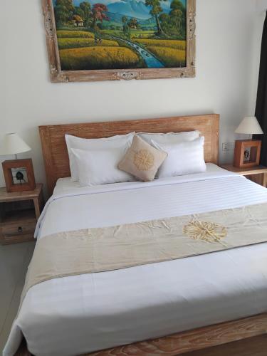 a bedroom with a white bed with a painting on the wall at Sujiwa Ubud Hotel & Villa in Ubud