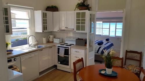 Una cocina con gabinetes blancos y una mesa en ella. en Victorian Beachfront Apartment with Ocean Views - The Coachhouse, en Narrabeen