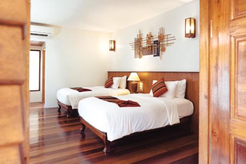 two beds in a room with white walls and wood floors at Maikaew Damnoen Resort in Damnoen Saduak