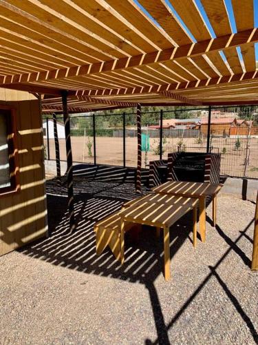 a wooden bench sitting under a wooden pergola at Cabaña con tinaja privada in Vicuña