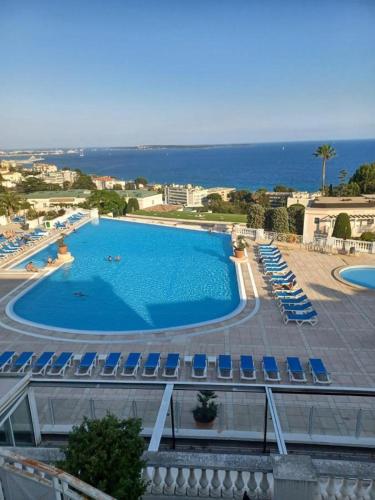 une grande piscine avec des chaises bleues et l'océan dans l'établissement Le cannois, à Cannes