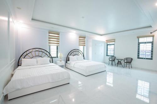 two beds in a white room with white floors and windows at King Hotel Hải Phòng in Hai Phong