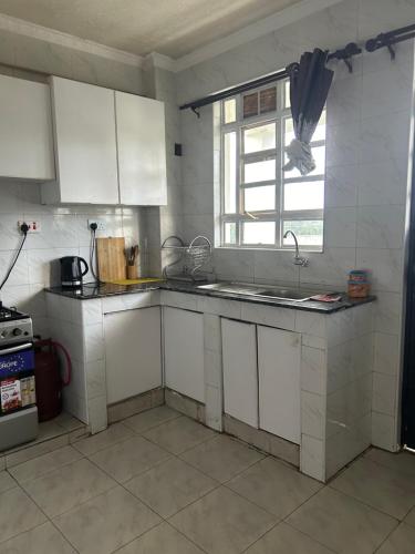 a kitchen with white cabinets and a sink and a window at Teakwood in Eldoret