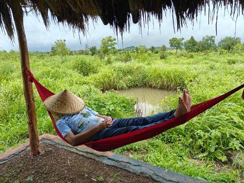 a man laying in a hammock in a field at Vana The Forest Farm in Saralgaon
