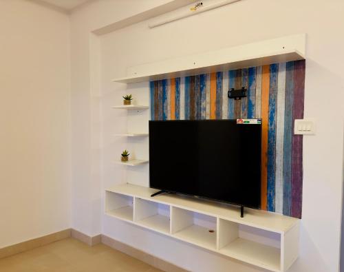 a flat screen tv on a white shelf in a room at Veu Ragamalika Apartment with Fully Equipped Kitchen, Balcony & Caretaker in Cochin