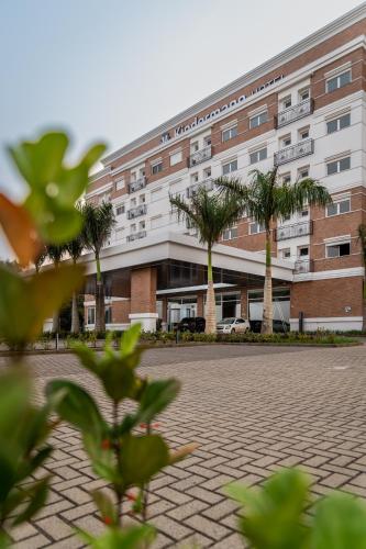 a building with palm trees in front of it at Hotel Kindermann Chapecó - Hotel Novo in Chapecó