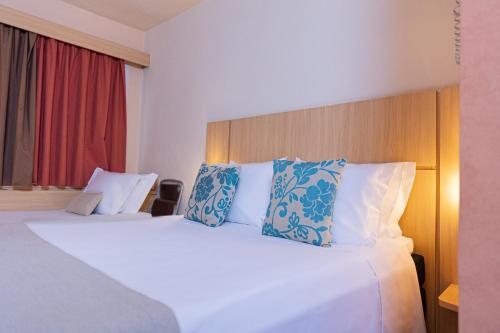 a hotel room with a bed with blue and white pillows at Hotel Lieto in Poços de Caldas