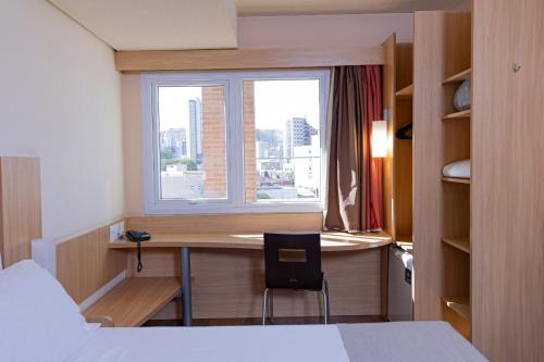 a hotel room with a desk and a window at Hotel Lieto in Poços de Caldas