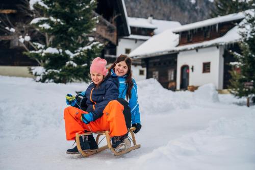 two girls riding on a sled in the snow at Slow Travel Resort Kirchleitn in Bad Kleinkirchheim