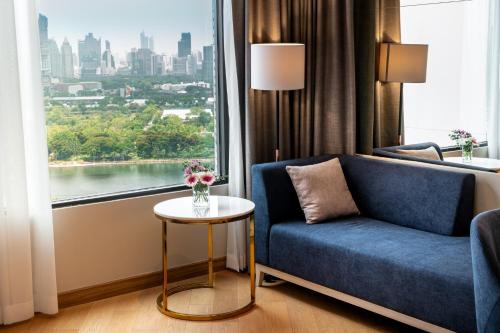 a living room with a blue couch and a large window at Rembrandt Hotel Bangkok in Bangkok