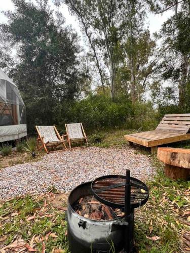 a fire pit with two chairs and a table and a tent at Magia Glamping, Domo Full Moon, entre las sierras y el mar in Punta Colorada