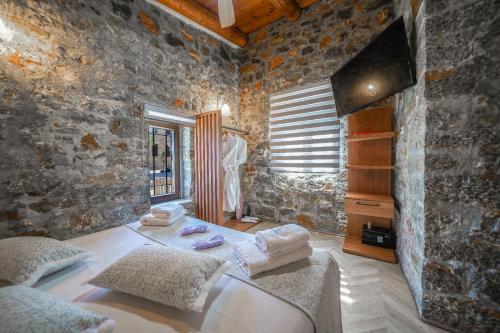 a stone walled bedroom with two beds and a television at Petra Elounda Suites - Adults Only in Elounda