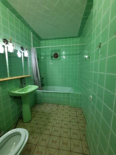 a green tiled bathroom with a toilet and a sink at Palm Hostel in Batumi