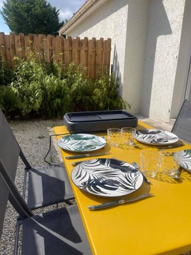 une table jaune avec des assiettes et des verres à vin dans l'établissement Maisons Martigny B - Proche Futuroscope et Aquascope, à Chasseneuil-du-Poitou