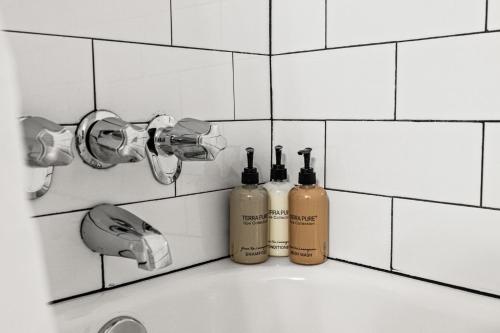 a white tiled bathroom with two bottles on a sink at Littlefield Lofts, Hosted by Placemakr - 6th St in Austin