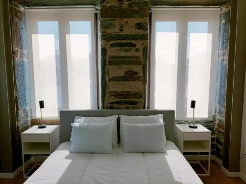Un dormitorio con una cama blanca con dos ventanas. en Valley Apartamentos T1, en Vila Nova de Foz Cõa