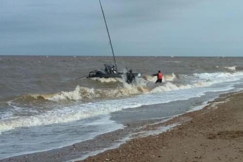 a man standing in the ocean with a fishing boat at The Patch at Snettisham Beach in Snettisham