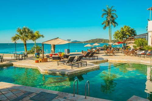 a swimming pool with chairs and tables and the ocean at Hotel Villareal São Francisco do Sul in São Francisco do Sul