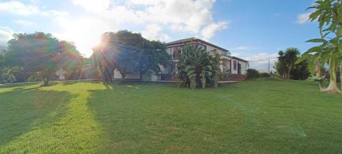 a house on a lawn with the sun behind it at Moradia da Graça Guesthouse in Praia da Vitória