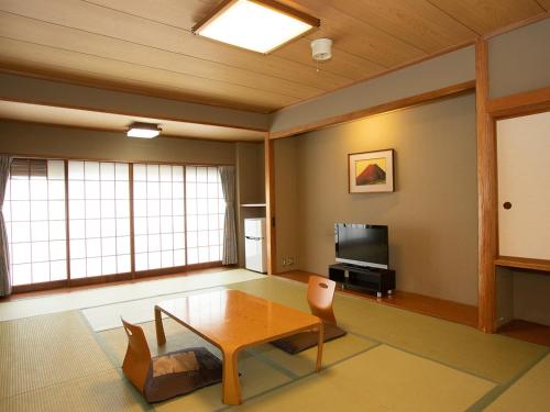 a living room with a table and a tv at Hotel Suimeikan in Yamanouchi