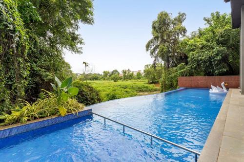 a swimming pool in the middle of a yard with trees at Radiant 1BHK Apartment by tisyastays in Candolim