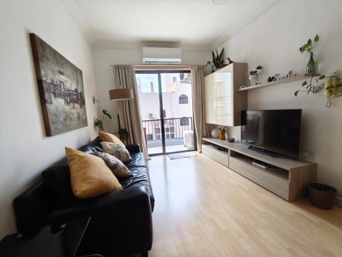 a living room with a black couch and a television at Gaia St Paul's Bay Modern Cosy Apartment Qawra Bugibba in St. Paul's Bay